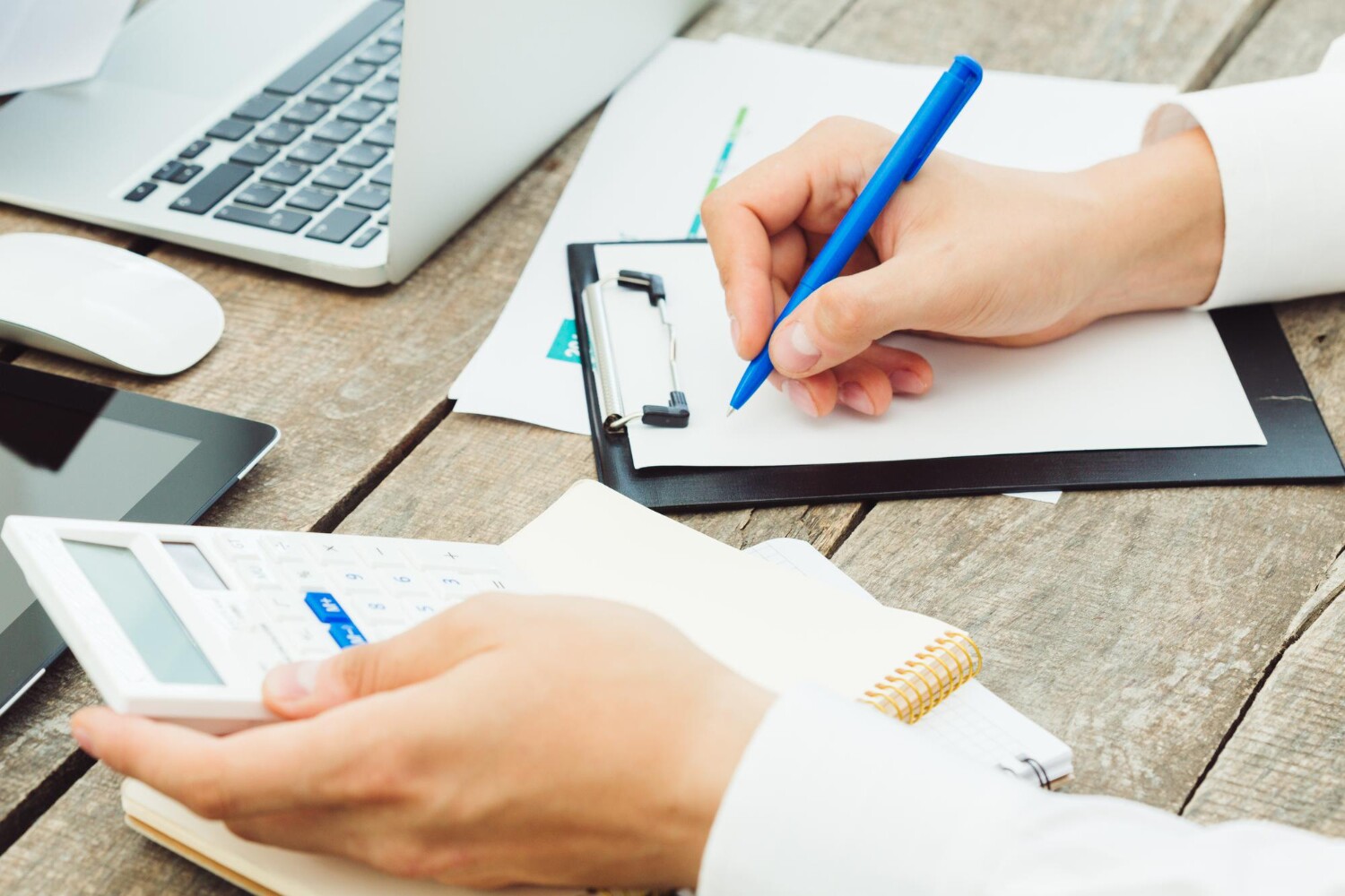 A person calculates with a calculator and pen while writing notes on a piece of paper.